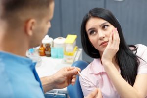 A woman holding her mouth and listening to a dentist.